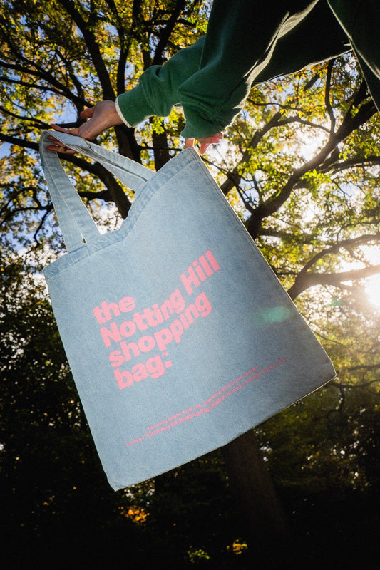 A notting hill shopping bag, in a park, in the basic denim style, light blue with pink writing