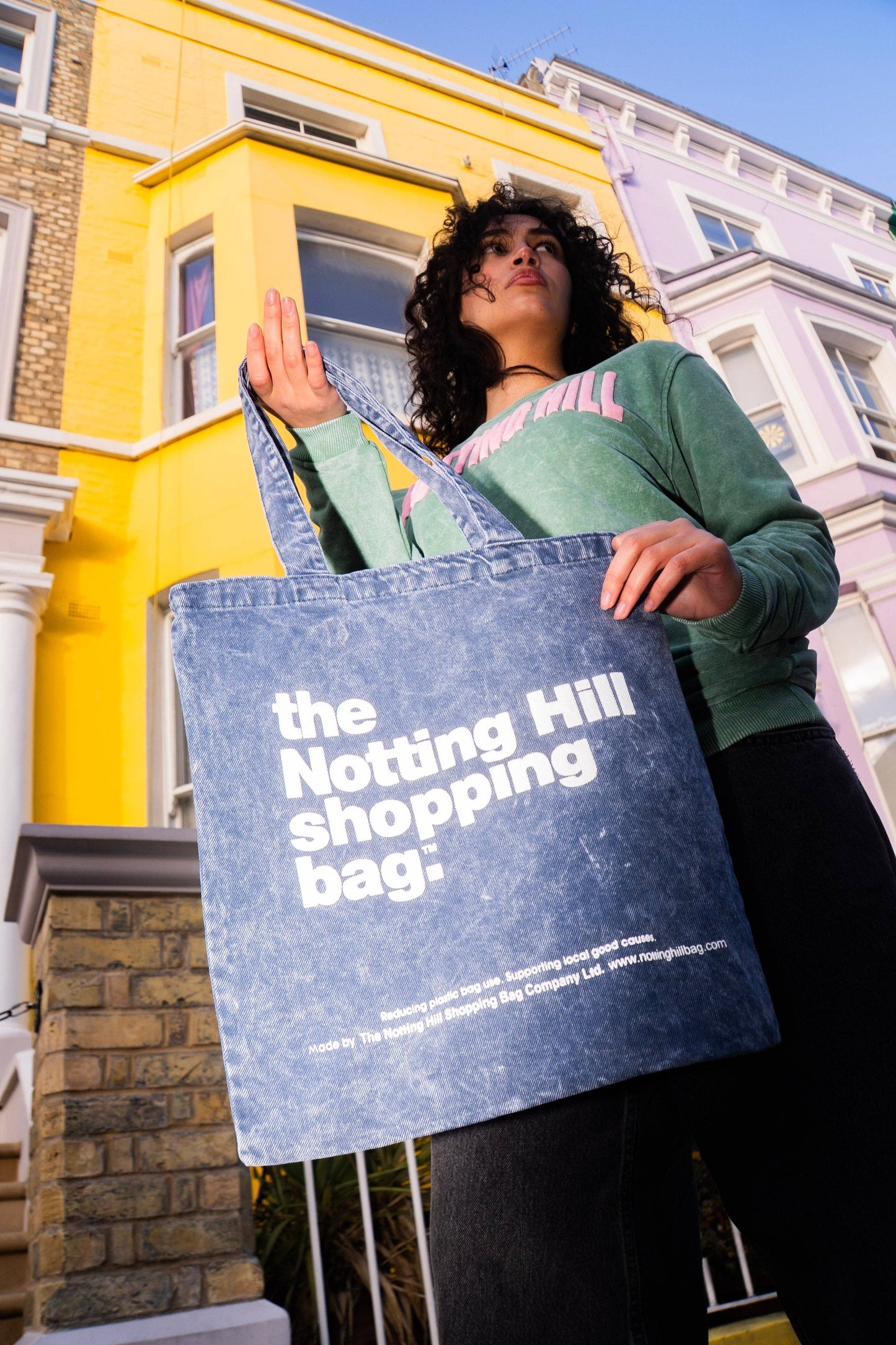 A Basic Denim Notting hill shopping bag, in blue denim with white writing, on portabello rd, notting hill