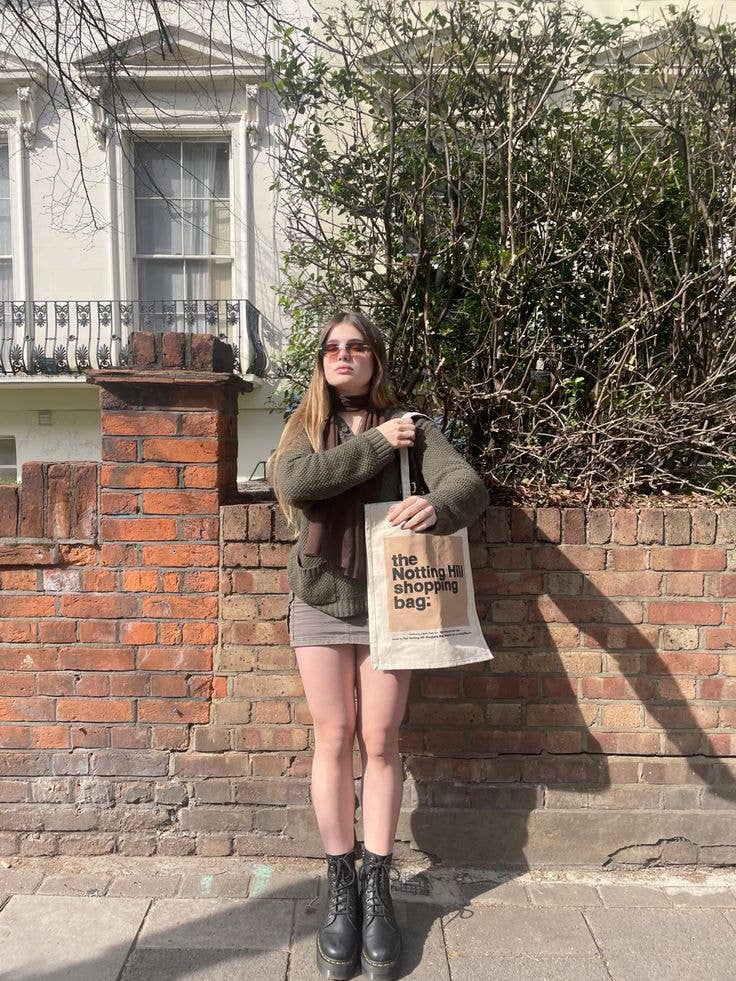 A girl in front of a brick wall, holding a Notting Hill Shopping Bag, Beige Colour block series bag