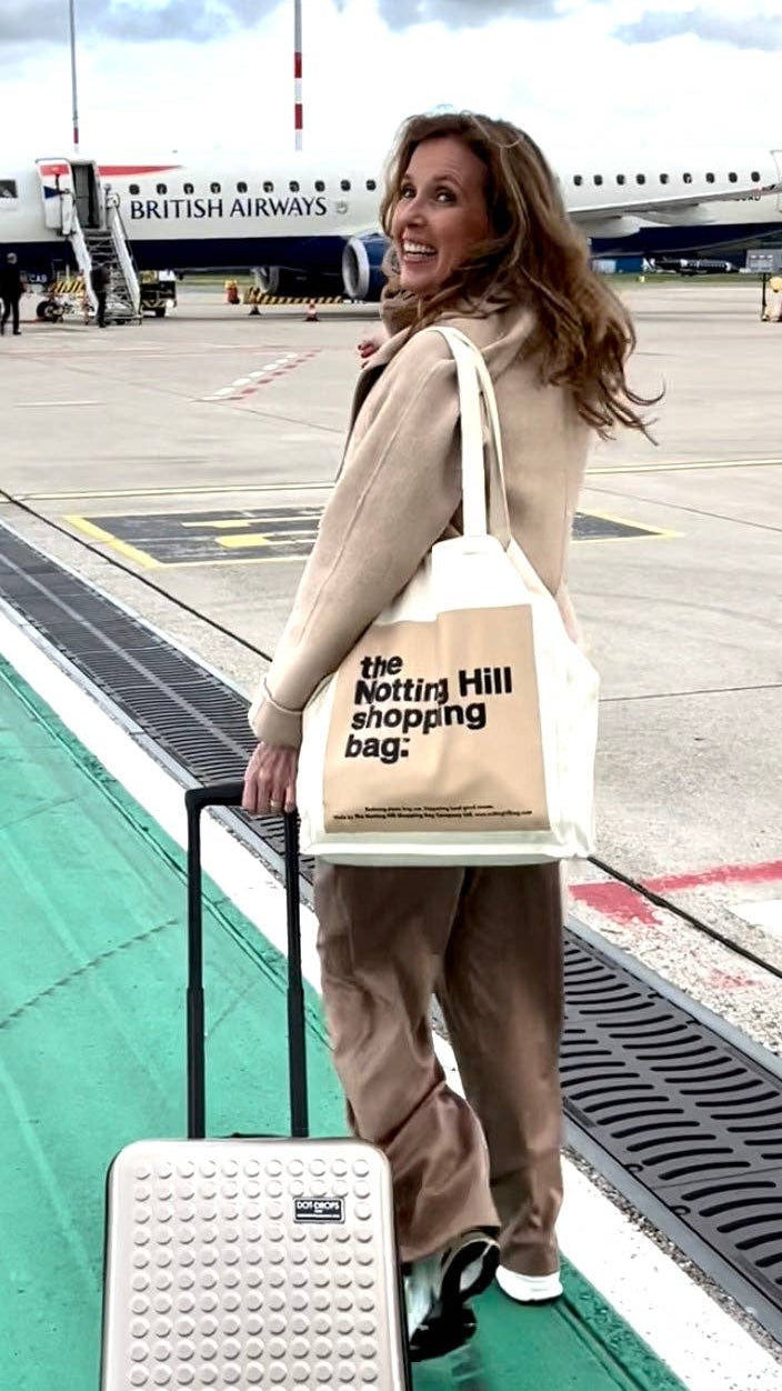 A woman getting on a plane, carrying a Notting Hill Shopping Bag, in the Beige Colour block range