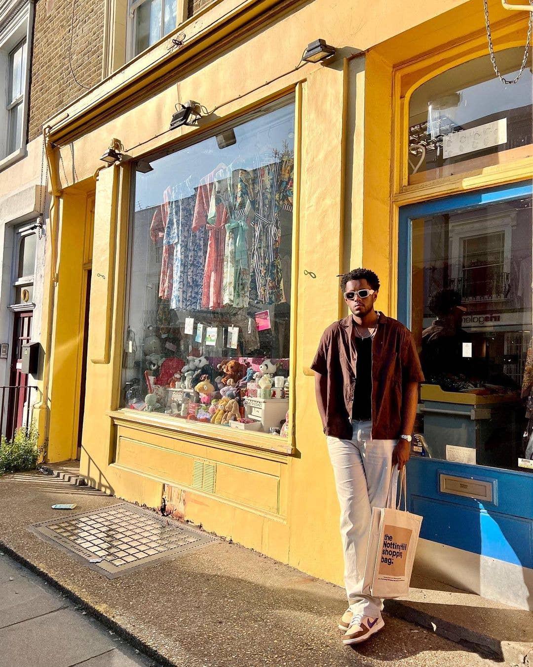 a Guy holding a Beige Colour Block series of the Notting Hill Shopping Bag, Infront of a shop on Portobello Rd, Notting Hill