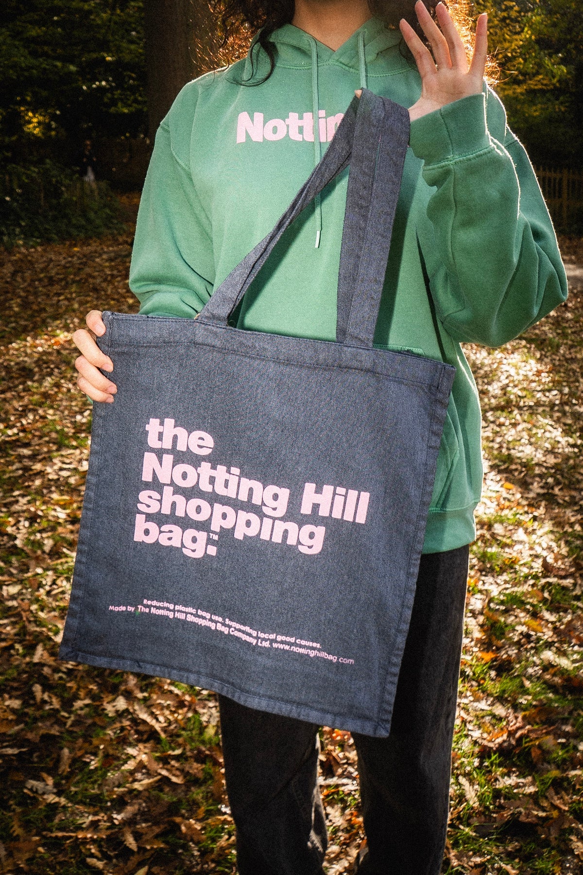 The Notting hill shopping bag hand dye collection in navy blue with pink writing held by a girl in a park