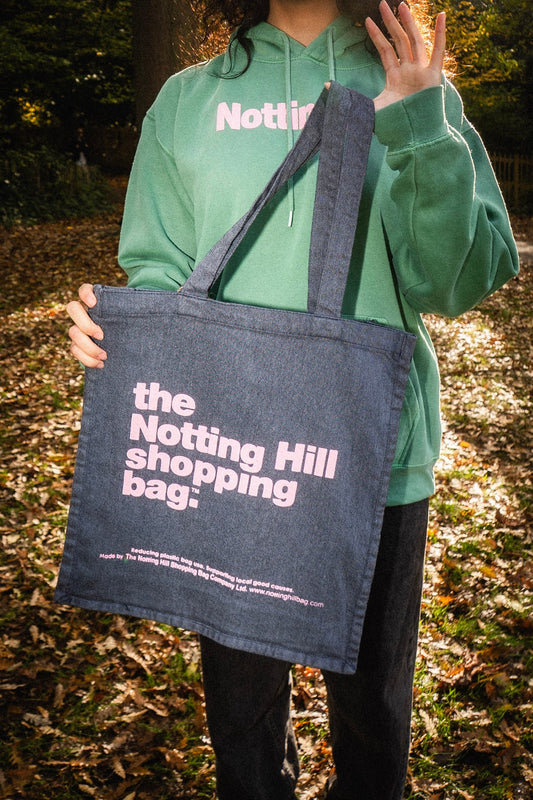 The Notting hill shopping bag hand dye collection in navy blue with pink writing held by a girl in a park