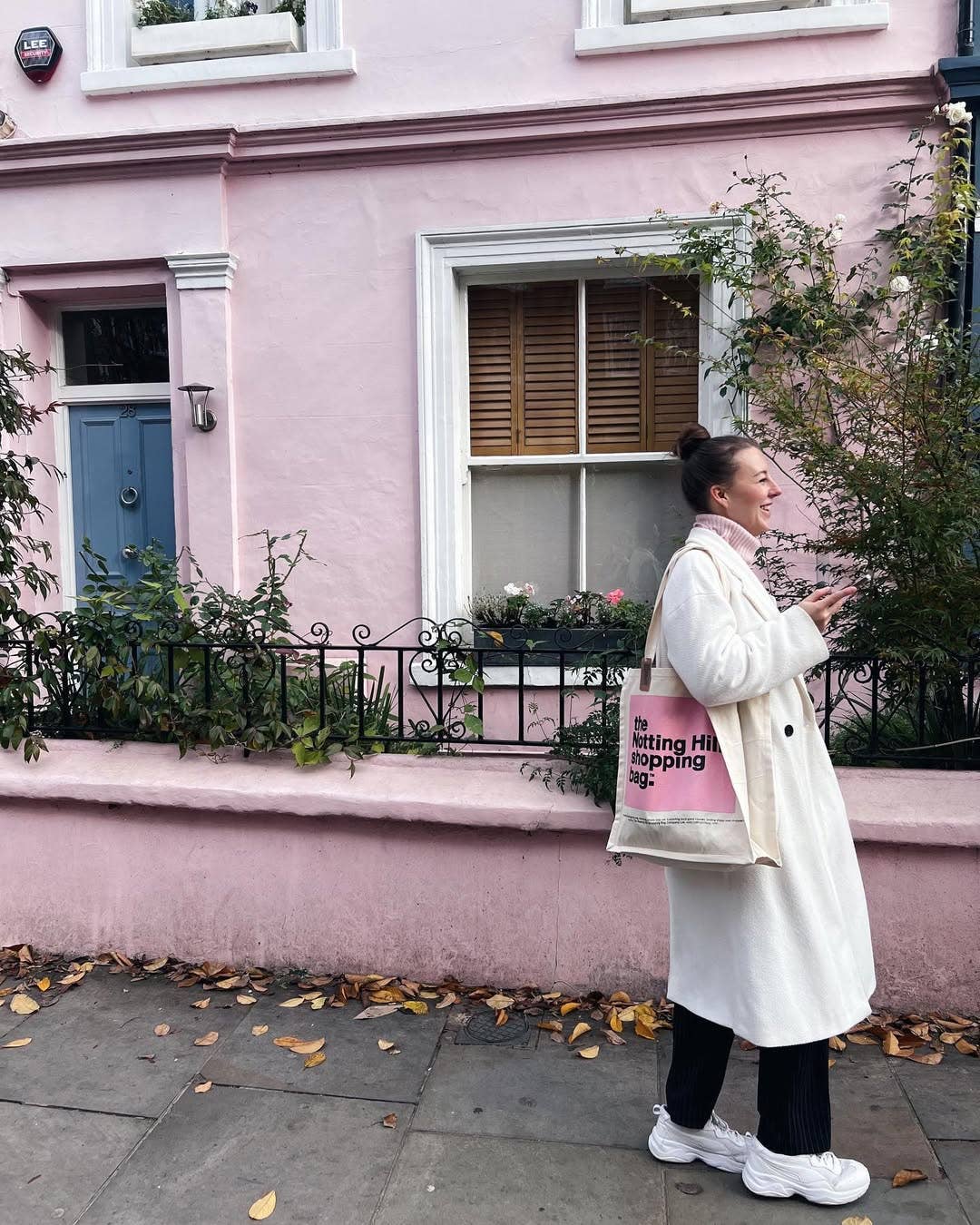 A woman walking with a Notting Hill Shopping Bag, Pink Colour Block range, Infront of a pink house