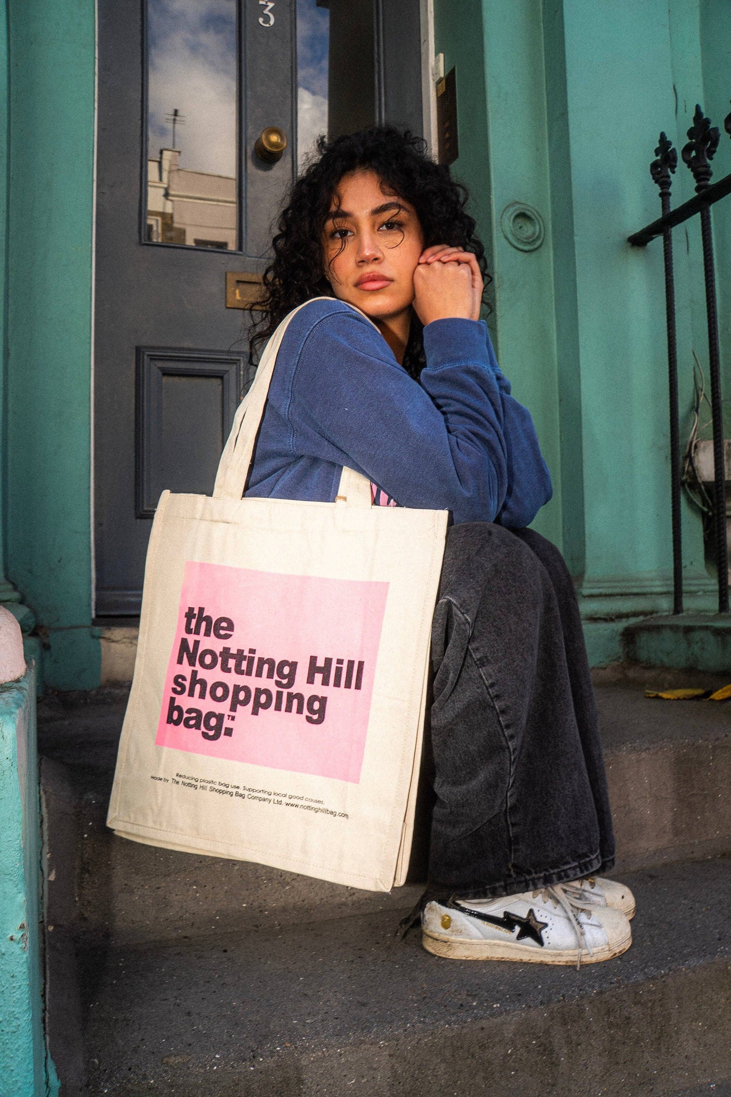 a girl on a step, holding a Notting hill shopping bag, color block range, in Pink