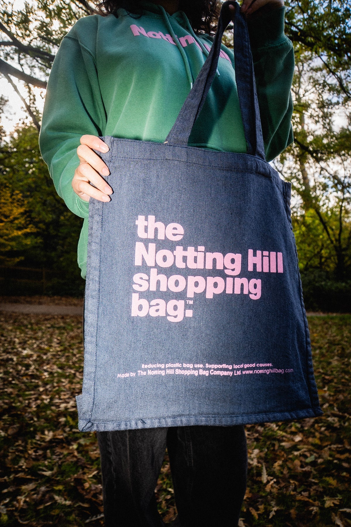 The Notting Hill Shopping Bag Hand dye collection, in Navy blue with pink writing held in a park by a woman