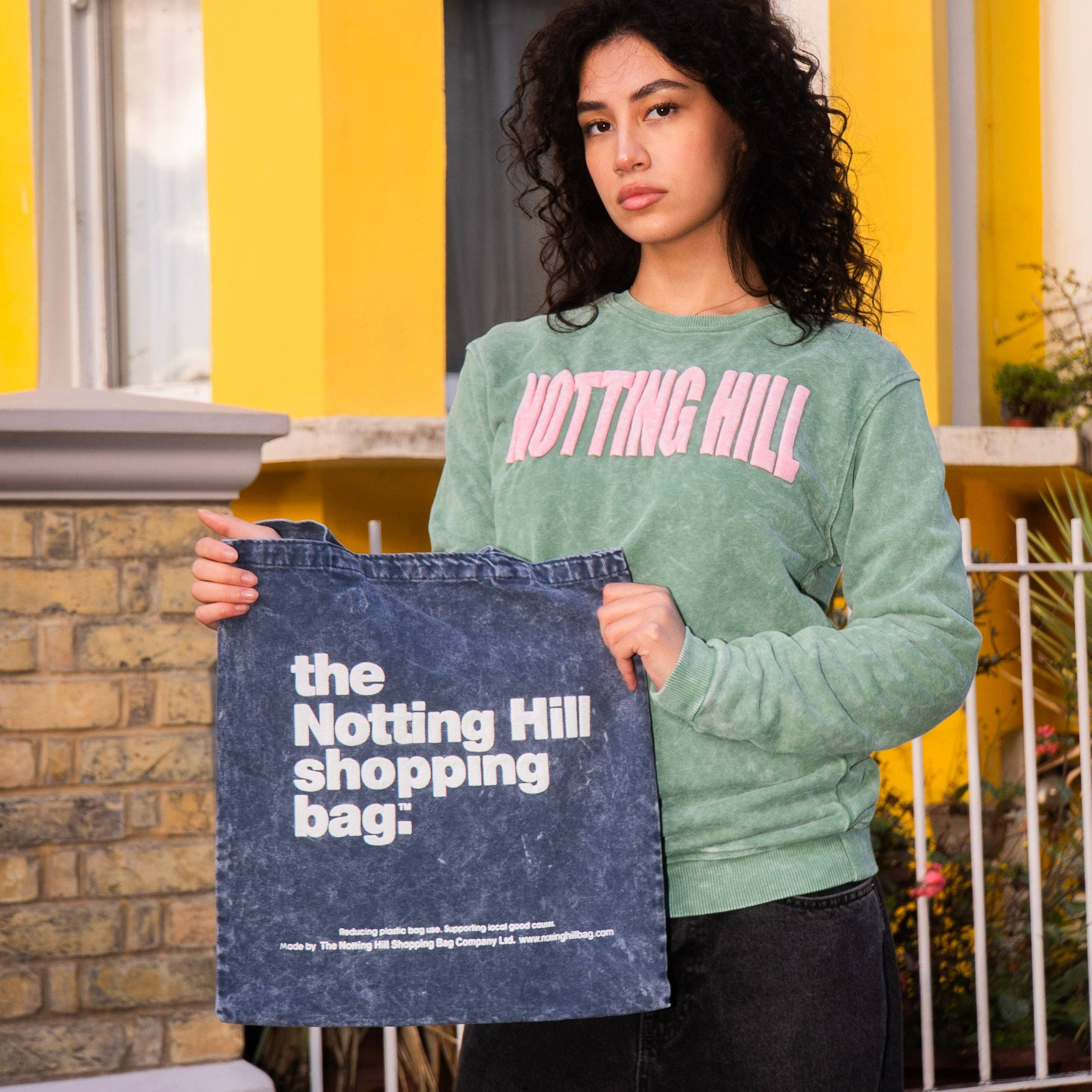 Woman holding Notting Hill Shopping bag on a london street. featured bag is The Notting Hill Shopping Bag Basic Denim Collection tote bag