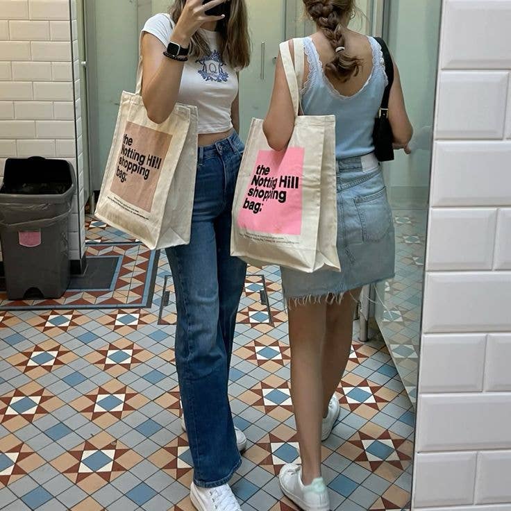 Two girls holding Notting Hill Shopping Bags, in the colour block range. one is a pink colour block and the other is a beige colour block
