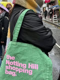 A Notting Hill Shopping Bag, from the hand dye collection, in green with pink logo, on a woman's shoulder