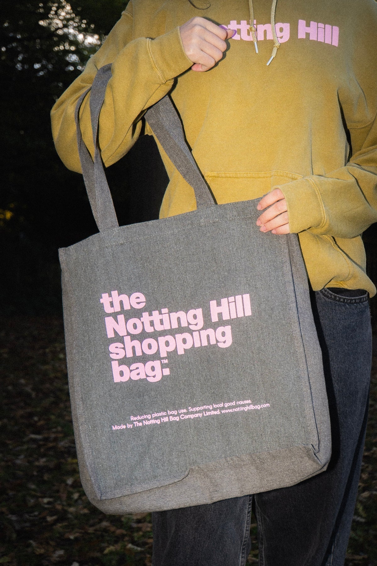 a woman in a park, holding a Notting Hill Shopping Bag , from the hand dye collection, in Grey with Pink logo, close up